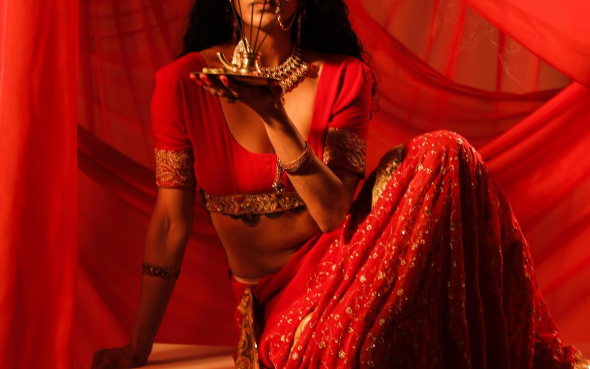 A beautiful Indian woman sitting gracefully, holding incense in a red sari.